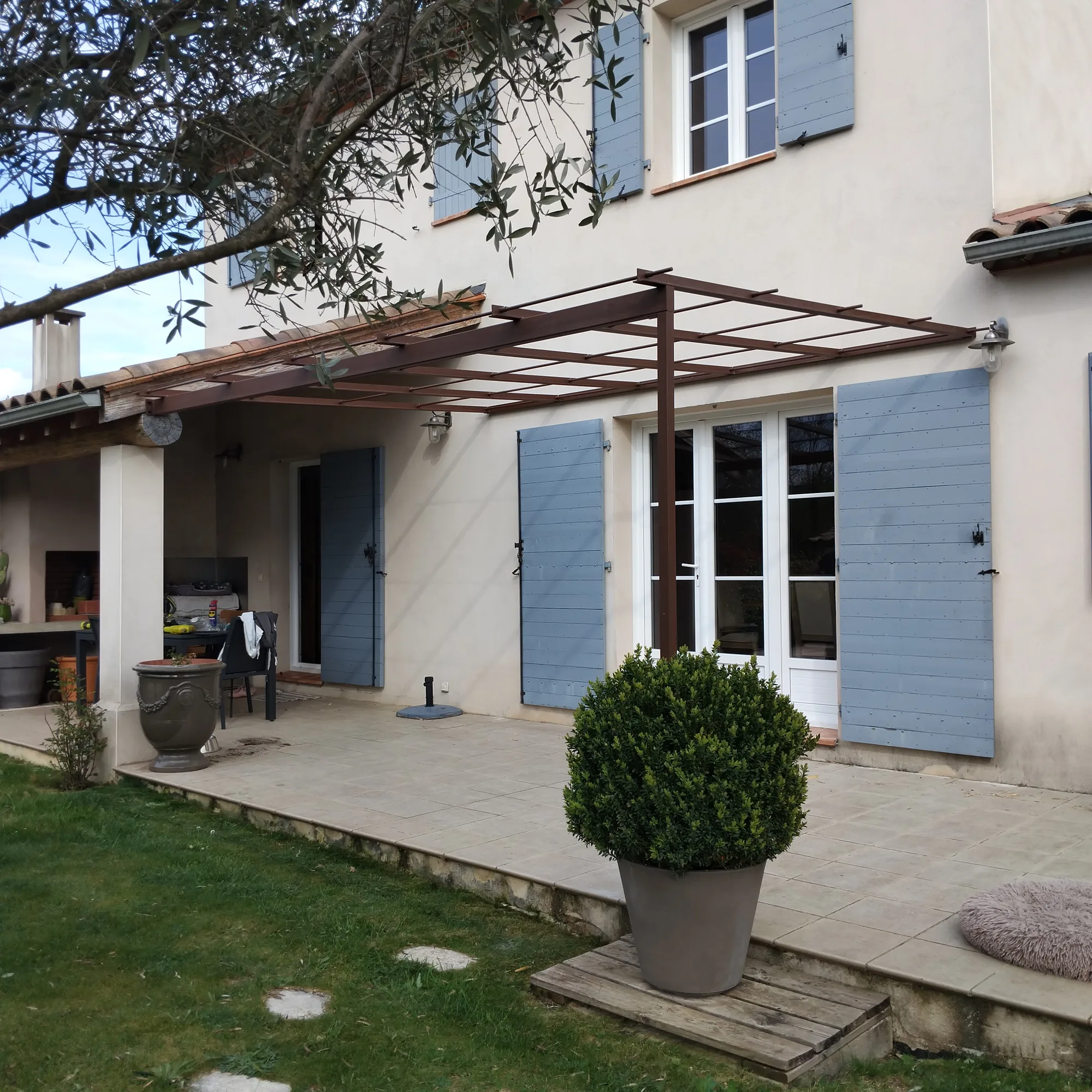 Pergola adossée en acier à lattage, posée contre une façade